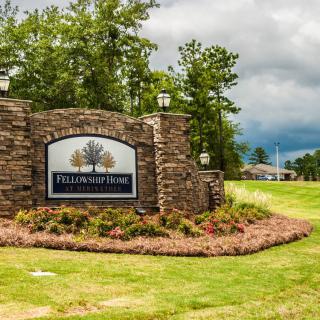 Entrance sign of a neighborhood surrounded by greenery and stone pillars.