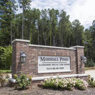 Entrance sign for Marshall Pines Alzheimer's Special Care Center, surrounded by trees and landscaping.