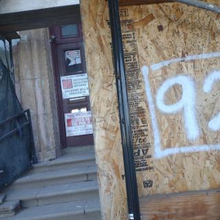 A boarded-up entrance to an abandoned building, featuring graffiti and a faded number on the wooden panel.