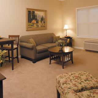 A cozy living room with a sofa, tables, and a lamp, decorated with a painting on the wall.
