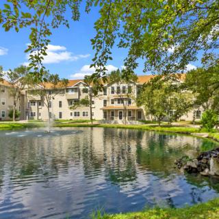 A serene residential building surrounded by a picturesque pond and lush greenery.