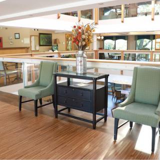 A modern lobby area with green chairs and a decorative table featuring a vase of flowers on a wooden floor.