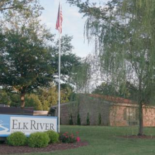 Welcome sign for Elk River with a flag and surrounding greenery.