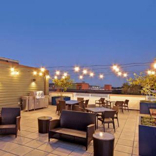 A cozy rooftop patio illuminated by string lights, featuring comfortable seating arrangements with a view of the evening sky.