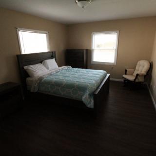 A cozy bedroom with a bed, chair, and windows letting in natural light.