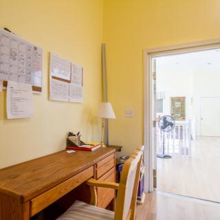 A cozy home office with a wooden desk and chair against a yellow wall, featuring documents pinned on the wall.