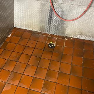 Industrial kitchen floor with a red hose and central drain.