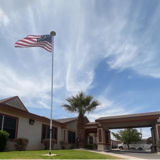 An American flag waves proudly in front of a building on a sunny day with scattered clouds.