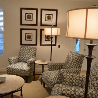 A cozy living room with patterned armchairs, a floor lamp, and framed artwork on the wall.