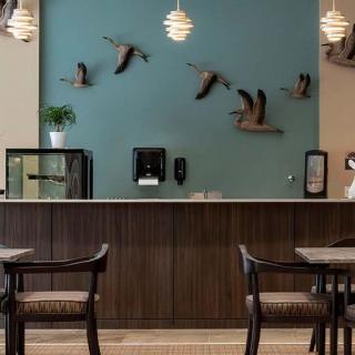 A stylish cafe interior featuring a modern counter, elegant lighting, and decorative wall art depicting birds in flight.