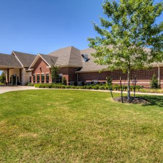A large residential house with a well-maintained lawn and trees on a sunny day.