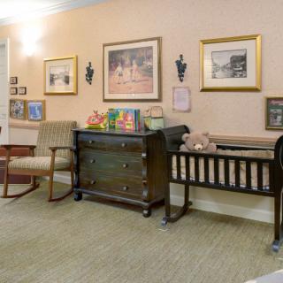 A cozy nursery room featuring vintage furniture, including a crib and rocking chair, adorned with framed photographs and paintings on the walls.