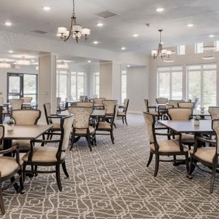 Elegant dining room with multiple tables and chairs, featuring decorative lighting and patterned carpeting.