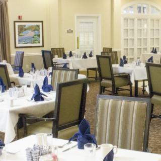 A well-appointed dining room with neatly arranged tables and chairs, featuring elegant table settings with folded napkins.