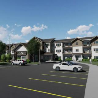 A modern residential building with a parking lot and cars under a clear blue sky.