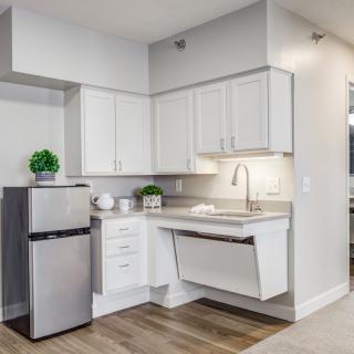 A modern, minimalist kitchen featuring white cabinets and a small stainless steel fridge.
