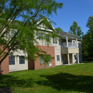 A residential apartment building with a well-maintained lawn and surrounding trees on a sunny day.