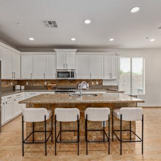 A spacious modern kitchen featuring white cabinets, a granite countertop, and comfortable bar stools.