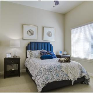 A cozy bedroom with a patterned bedspread and blue headboard beside a window with blinds.