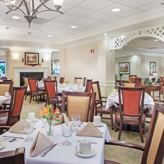 An elegant dining room setup with neatly arranged tables and chairs, adorned with flowers and folded napkins.