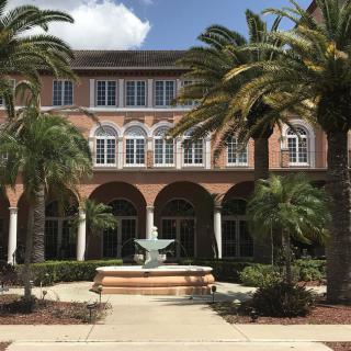 A Mediterranean-style building surrounded by palm trees and featuring a central fountain in the courtyard.