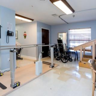 A physical therapy room equipped with parallel bars, a wheelchair, and various exercise equipment.