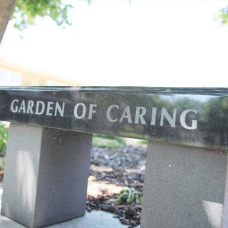 A memorial bench engraved with 'Garden of Caring' located outdoors in a garden setting.