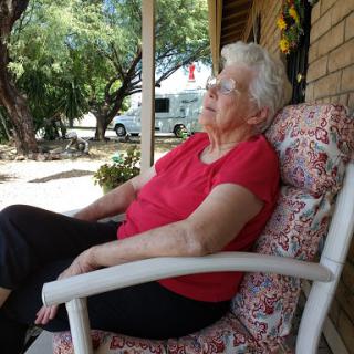An elderly woman enjoys a peaceful moment on the porch, soaking in the warmth of a sunny day.