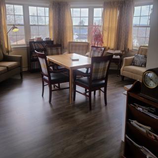 A cozy living room with a dining table set surrounded by armchairs and large windows.