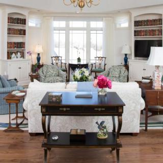 A classic living room with elegant furnishings, featuring bookshelves, a central sofa, and large windows.
