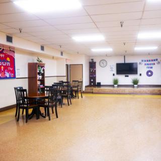 An empty indoor community center with chairs, tables, and a small stage area.