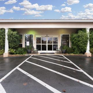 Front entrance of a building with a parking lot and cloudy sky in the background.