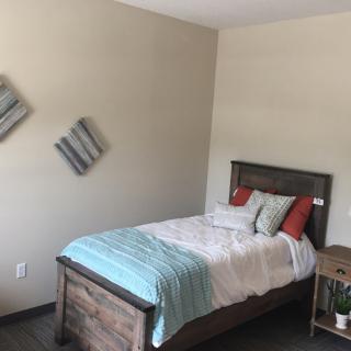 A minimalist bedroom with a single bed, accented by colorful pillows and wall art.