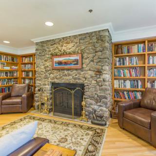 A cozy library room with bookshelves lining the walls, a stone fireplace, and comfortable leather armchairs.