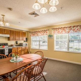 A cozy kitchen and dining area featuring wooden cabinetry, a dining table with chairs, and large windows with floral curtains.