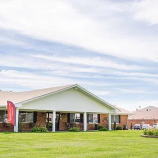 A single-story brick building with a large lawn and a partly cloudy sky.