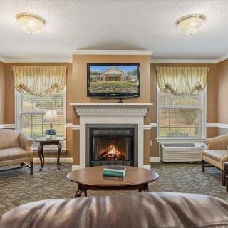 A cozy living room featuring a fireplace and a television mounted above it, surrounded by comfortable seating and large windows.