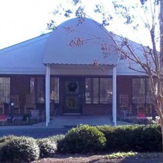 A small brick building with an awning over the entrance, surrounded by shrubs and trees.