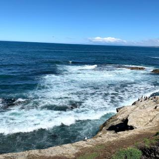 A beautiful coastal view with waves crashing against the rocks under a clear blue sky.
