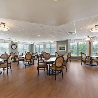 A spacious dining area with tables and chairs, featuring large windows and wooden flooring.