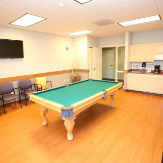 A recreation room with a billiards table, seating area, and kitchenette.