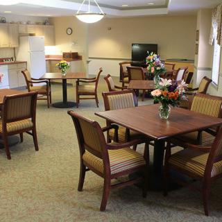 A well-lit dining area with tables and chairs, featuring floral centerpieces and a television.