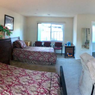 A cozy bedroom featuring two beds with patterned covers, a window allowing natural light, and comfortable seating.