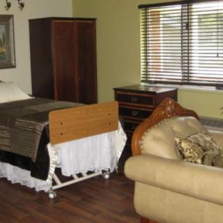 A room with a hospital bed, sofa, and wooden furniture, featuring window blinds and a wooden floor.