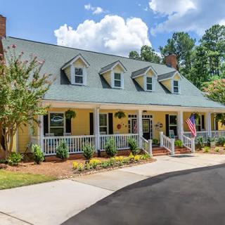 A charming yellow house with a spacious front porch and landscaped yard.
