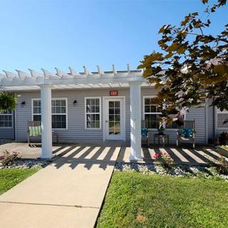 A bright, sunny day highlights the front of a house with a pergola-covered porch and well-maintained landscaping.