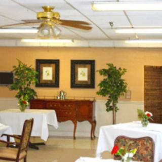 A neatly arranged dining area with tables covered in white cloths, decorated with plants and framed artworks on the wall.
