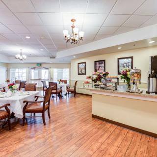 A spacious dining area with elegant chandeliers, neatly arranged tables and chairs, complemented by wood flooring and decorative wall art.