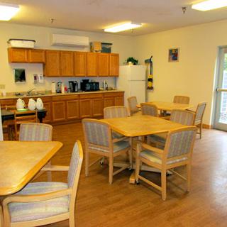 A cozy dining area featuring wooden tables and chairs, with a kitchen in the background.