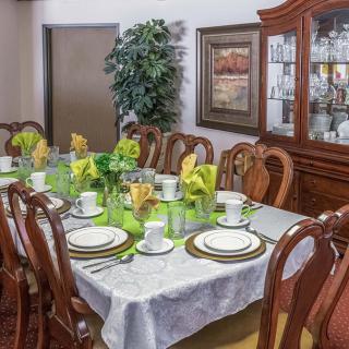 An elegantly set dining table with green and gold accents, surrounded by wooden chairs and a china cabinet in the background.